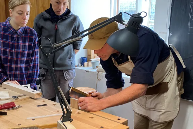 Slöjdlärare visar elever hur han arbetar med trä
